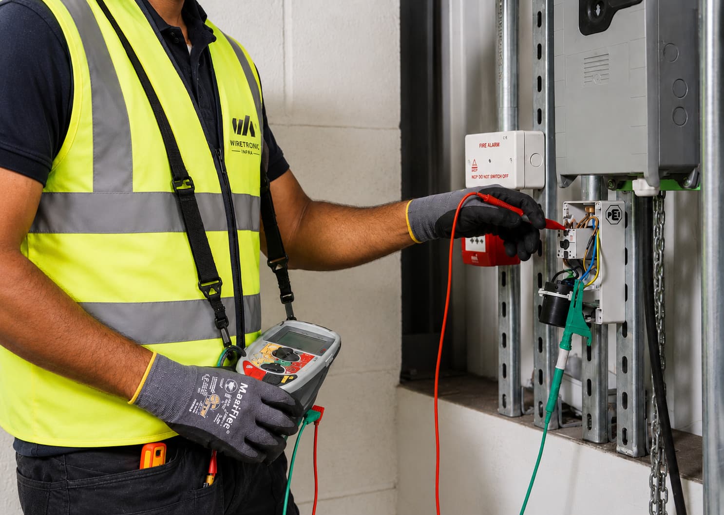 Wiretronic Infra technician testing an open electrical installation with red and green test leads