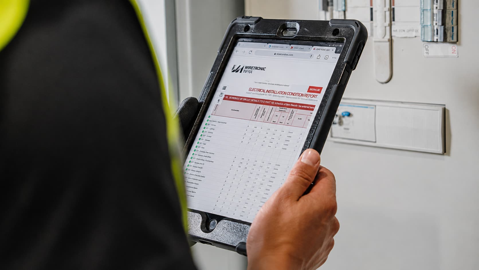 Engineer reviewing an electrical installation condition report on a rugged tablet showing Wiretronic Infra branding