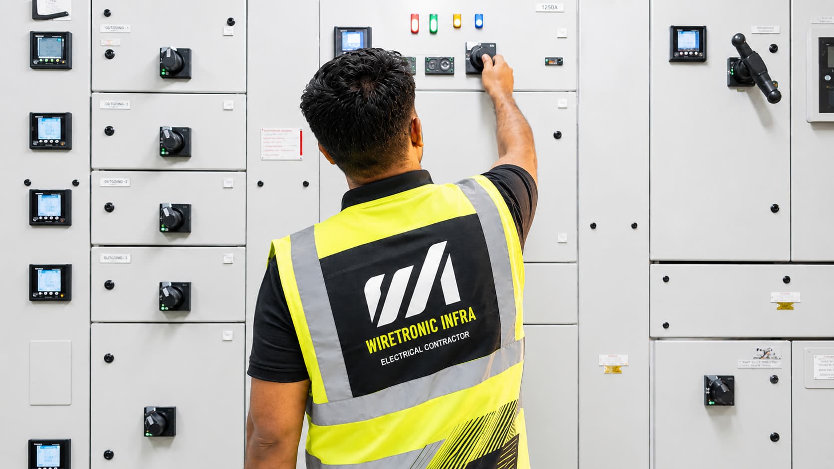 Wiretronic Infra engineer in branded safety vest operating a switchboard panel